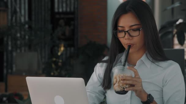 Asiatique attrayant jeune femme portant des lunettes, travaillant à son ordinateur portable dans la rue — Video