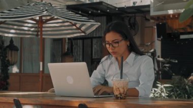 Asyalı çekici, gözlüklü, sokakta dizüstü bilgisayarıyla çalışan genç bir kadın.