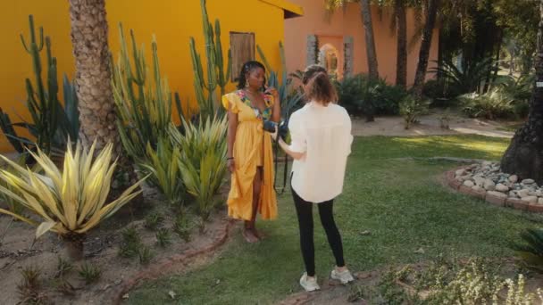 Um belo modelo preto posa para um fotógrafo. Moda elegante sessão de fotos em um jardim de cacto — Vídeo de Stock