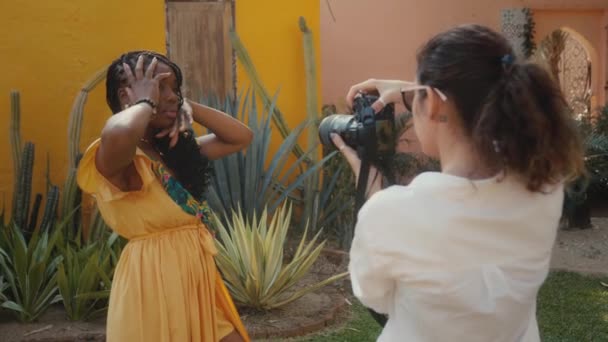 Een prachtig zwart model poseert voor een fotograaf. Stijlvolle fashion fotoshoot in een cactus tuin — Stockvideo