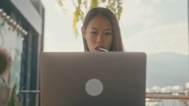 Молода азійка працює за своїм ноутбуком у кафе на даху в місті. — стокове відео