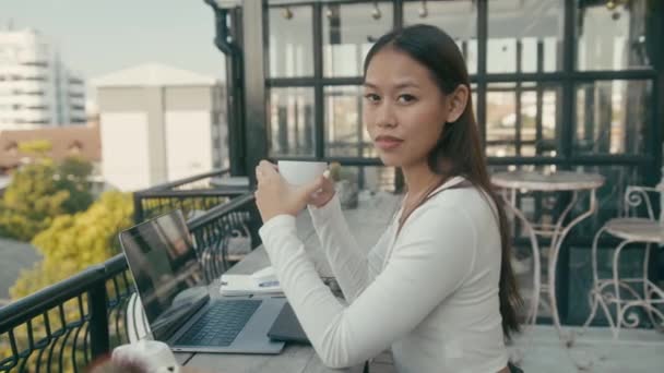 Egy fiatal ázsiai lány dolgozik a laptopjánál egy háztetőn a városban. — Stock videók
