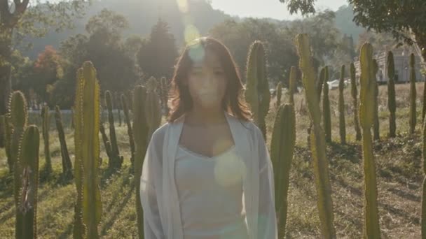 Молодая азиатка в кактусном поле на закате смотрит в камеру — стоковое видео