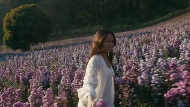 Ung asiatisk kvinna springer i blomma fält på solnedgången — Stockvideo