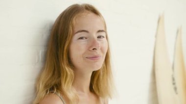 Fashion portrait of cute young woman with vitiligo pigmentation posing over white wall with surfboards, looking to camera