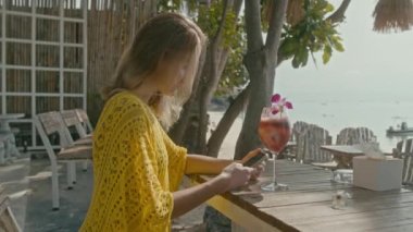 Vitiligo pigmentasyonu olan genç ve güzel bir kadın sahilde oturur, telefonda sohbet eder, ağır çekimde.