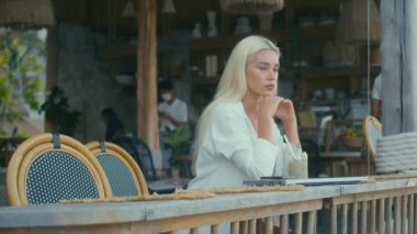Beyaz gömlekli sarışın kız kafede dizüstü bilgisayarla çalışıyor ve kameraya bakıyor. Bağımsız kavram