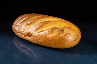 Beyaz ekmeğin uzun somunu mavileşerek masayı yansıtıyor. Beslenmenin siyah arka plandaki ürünleri