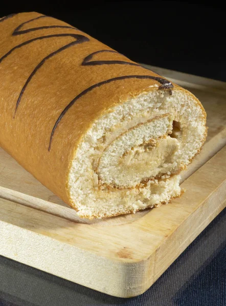 Mutfaktaki ahşap bir tahtanın üzerinde tatlı bir rulo. Gıda ürünleri siyah arka planda