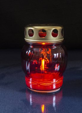 Candle blazes in glass form with metallic lid on dark background. Items for decorating the festive table