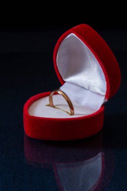 Masadaki kırmızı kutuda altın bir yüzük. Siyah arkaplanda mücevherler