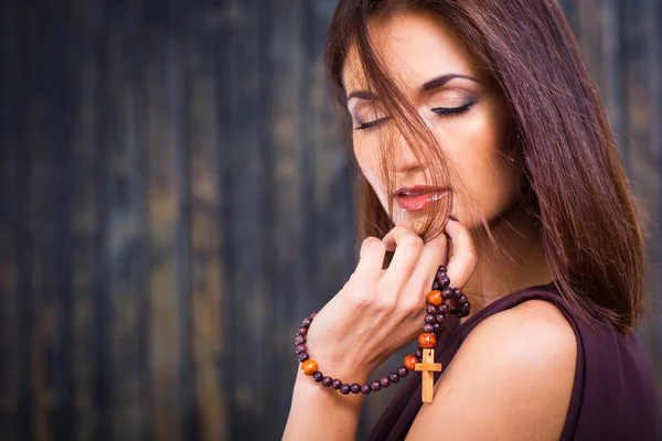 Hermosa chica con cuentas cristianas contra la vieja pared de madera — Foto de Stock