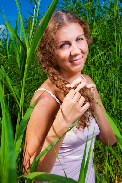 Krásná dívka pletení pletenec mezi vysokou trávou letní louky — Stock fotografie