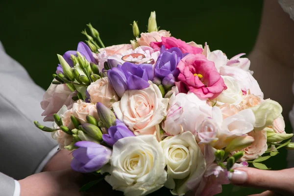 Hands of bride and groom holding wedding bouquet — Stock Photo, Image