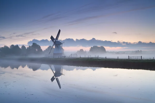 Белая голландская ветряная мельница у реки в тумане восхода солнца — стоковое фото