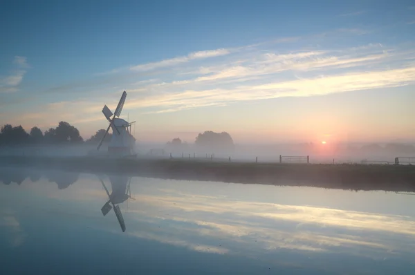 Molino de viento holandés por río durante el amanecer brumoso — Foto de Stock