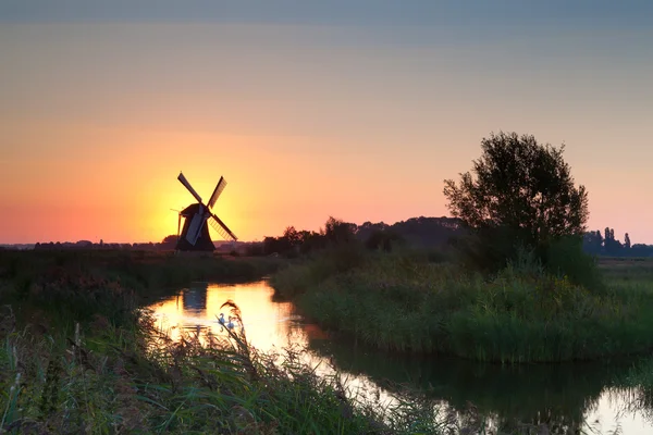 Lichtend windmolen tijdens zonsopgang boven de rivier — Stockfoto