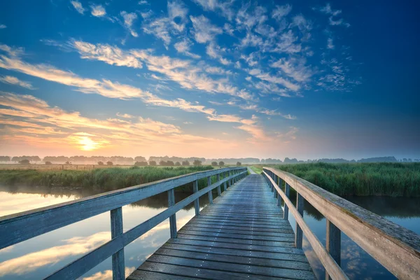 Puente de madera a través del río al amanecer — Foto de Stock