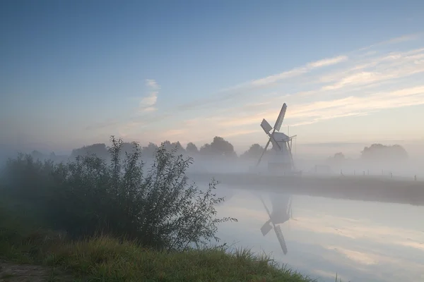 Ветряная мельница у реки в утреннем тумане — стоковое фото