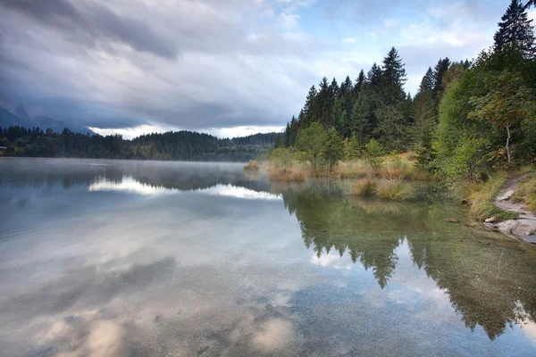 Mattina nebbiosa sul lago alpino nella foresta di conifere — Foto Stock