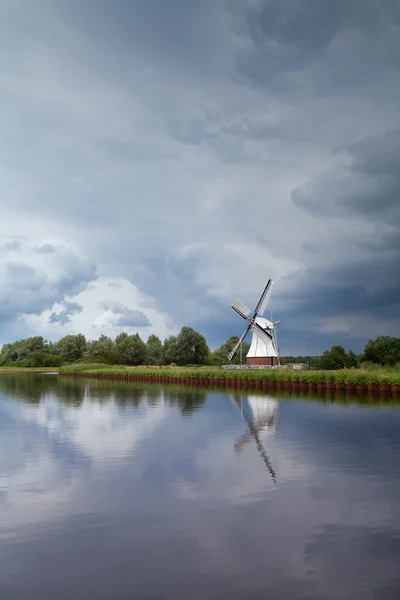 Ветряная мельница за рекой над туманным бурным небом — стоковое фото