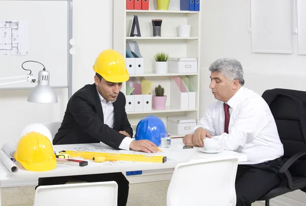 Arquitectos sentados a la mesa y mirando un proyecto — Foto de Stock