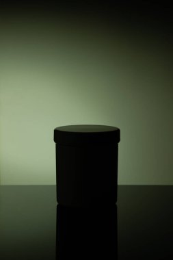 Low light white cosmetic jar with reflection on desaturated green background