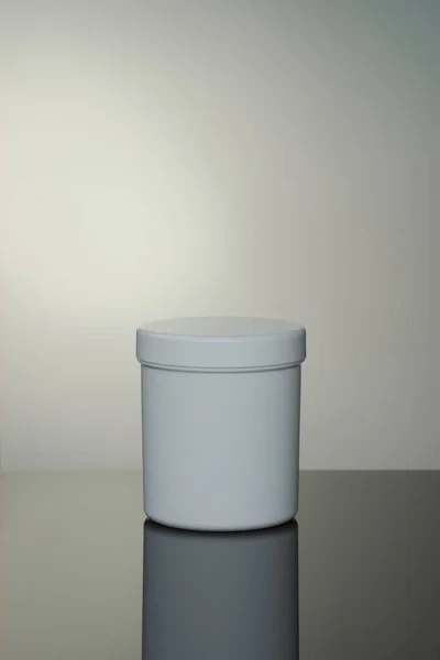 Low light white cosmetic jar with reflection on gray background, spot light on background, beauty care concept