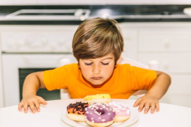 Kafkasyalı sarışın çocuk mutfak masasındaki dört renkli çöreğe bakıyor.