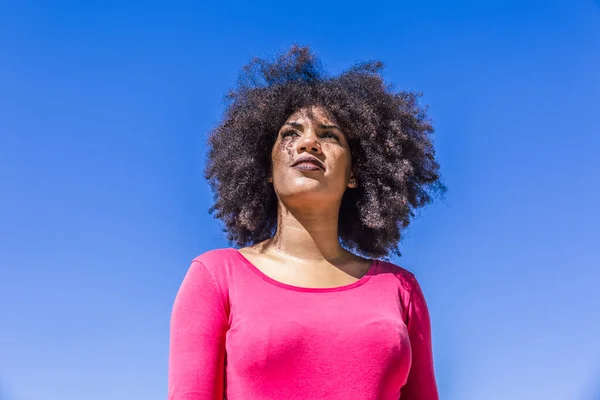 Racial woman with afro hair, looks with an air of freedom on a beautiful sunny day