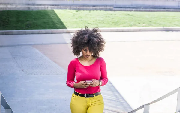 Attractive Afro Haired Brunette Woman Checks Her Mobile Phone While — Stock Photo, Image