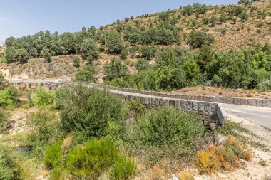 Yeşil ve sürdürülebilir bir manzaranın ortasından geçen taş köprü, güneşli bir gün.