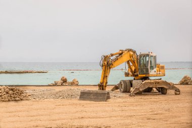 Sakin bir sahilde kazı makinesi inşaat için kum topluyor..