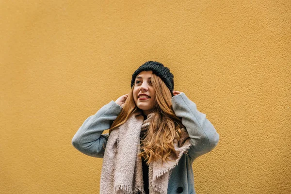 Blond young woman in scarf, hat and coat looks up with positivity and hope