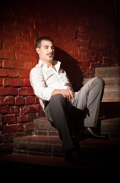 Businessman sitting on stairs near brick wall — Stock Photo, Image