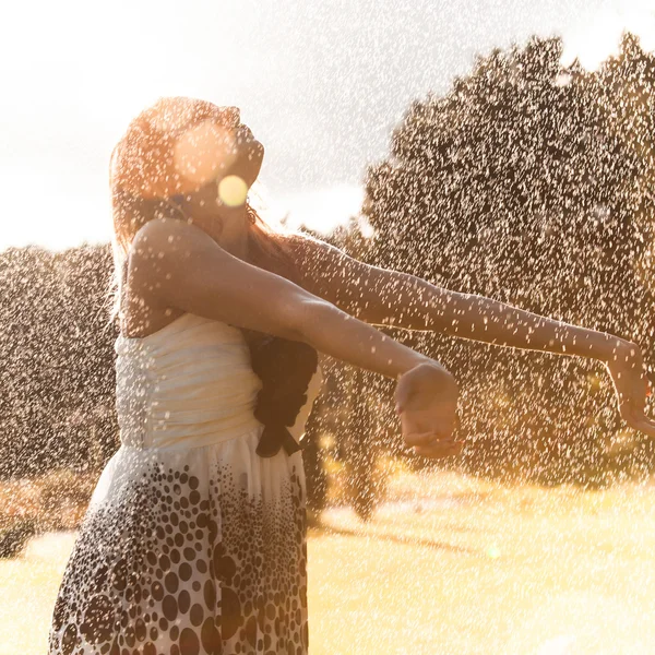 Girl catching drops of water from sprinkler — Stock Photo, Image