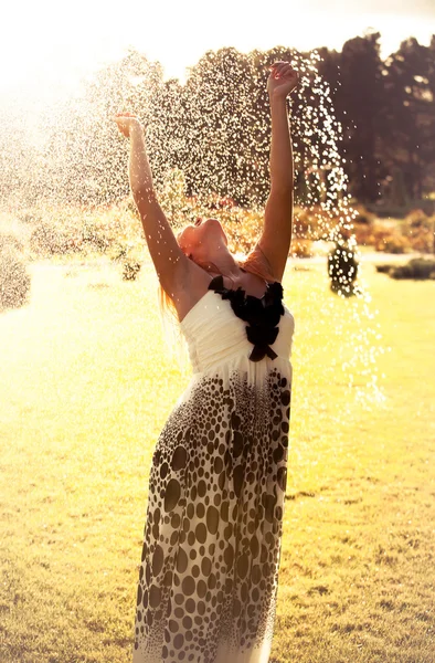Meisje permanent in waterdruppels op het gazon van de sprinkler — Stockfoto