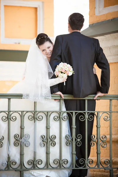 Groom sitting on railing while bride hugging him — Stock Photo, Image