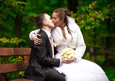 Genç gelin ve damat bankta oturan ve öpüşme