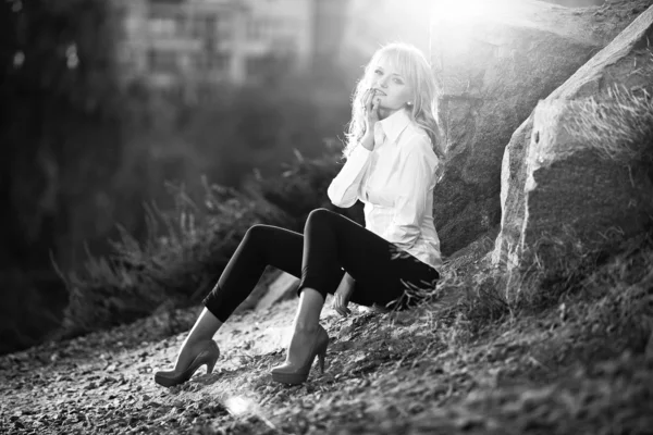 Sexy blonde girl sitting near big rock on top of mountain — Stock Photo, Image