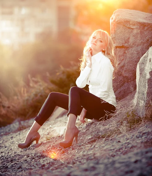 Sexy blonde girl sitting near big rock on hill — Stock Photo, Image