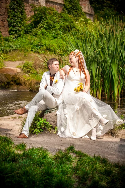 Appena sposati coppia seduta insieme su argine — Foto Stock