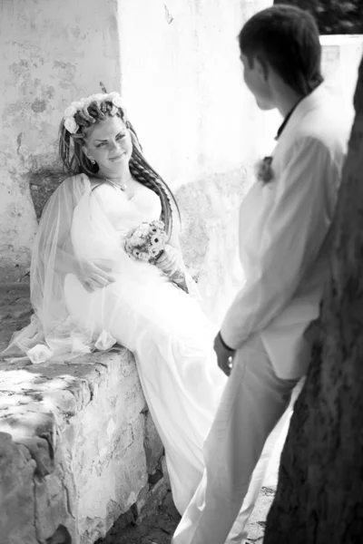 Young bride sitting near wall and looking at groom — Stock Photo, Image