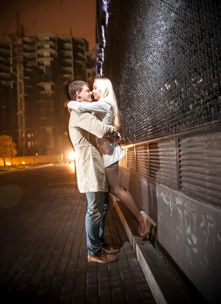 Jovem casal beijando à noite perto de parede preta — Fotografia de Stock