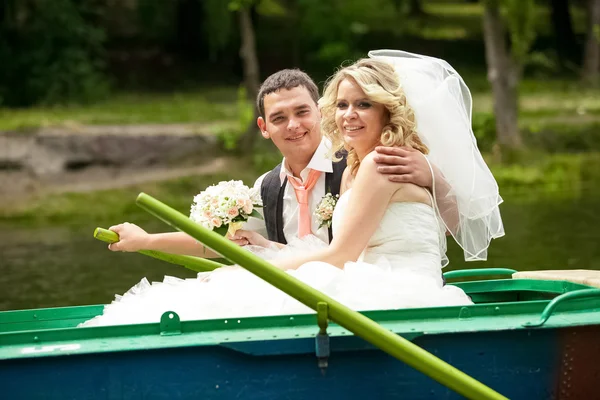 Smiling bride and groom riding on rowing boat on lake — Stock Photo, Image