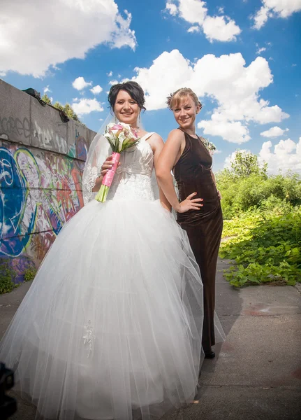 Bride standing in park with bridesmaid — Stock Photo, Image