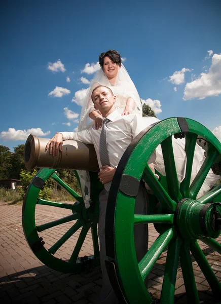 Bride sitting on old gun in fortress and hugging groom — Stock Photo, Image