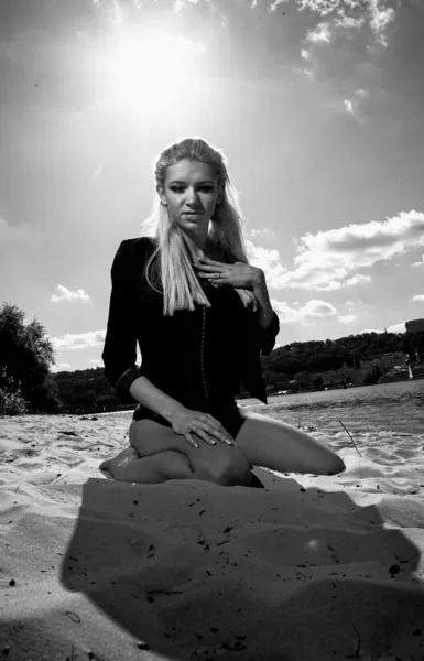 Retrato de menina sexy em casaco preto sentado nos joelhos na praia — Fotografia de Stock