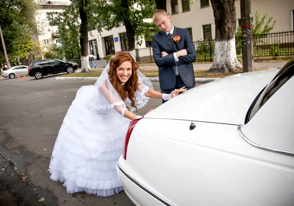 Bride pushing car while groom looking at her