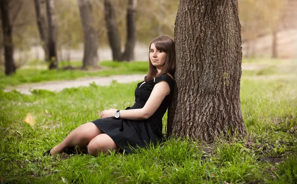 Chica morena tumbada bajo el árbol en vestido negro — Foto de Stock